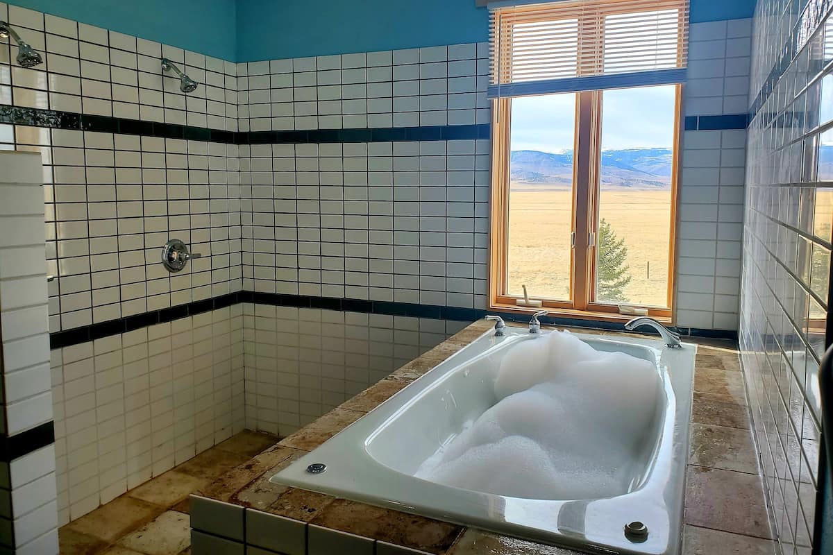 A bathroom with a bathtub, a window with a view of a desert landscape, and tiled walls.