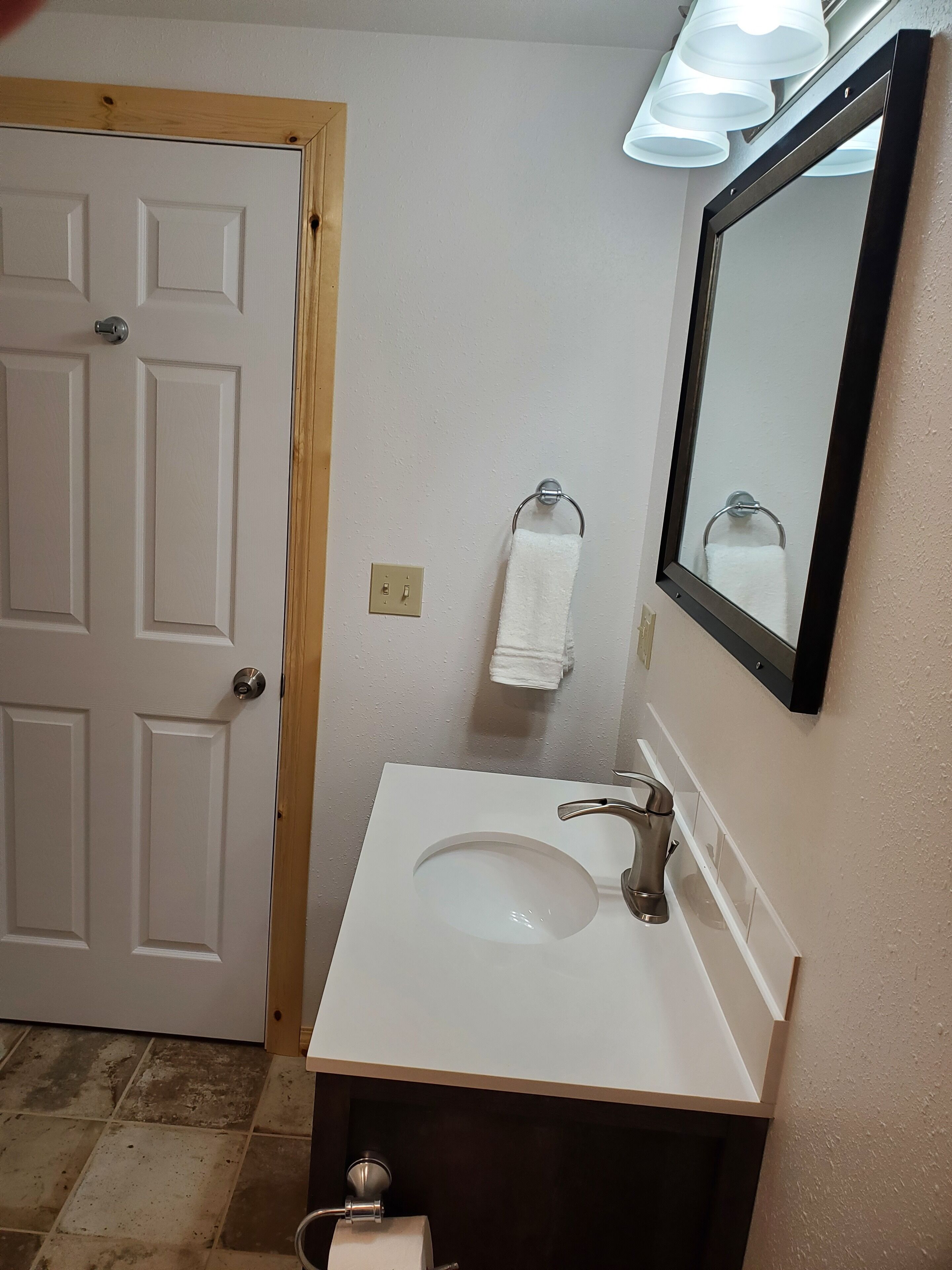 A bathroom with a white sink, a mirror, a towel rack, and a door.