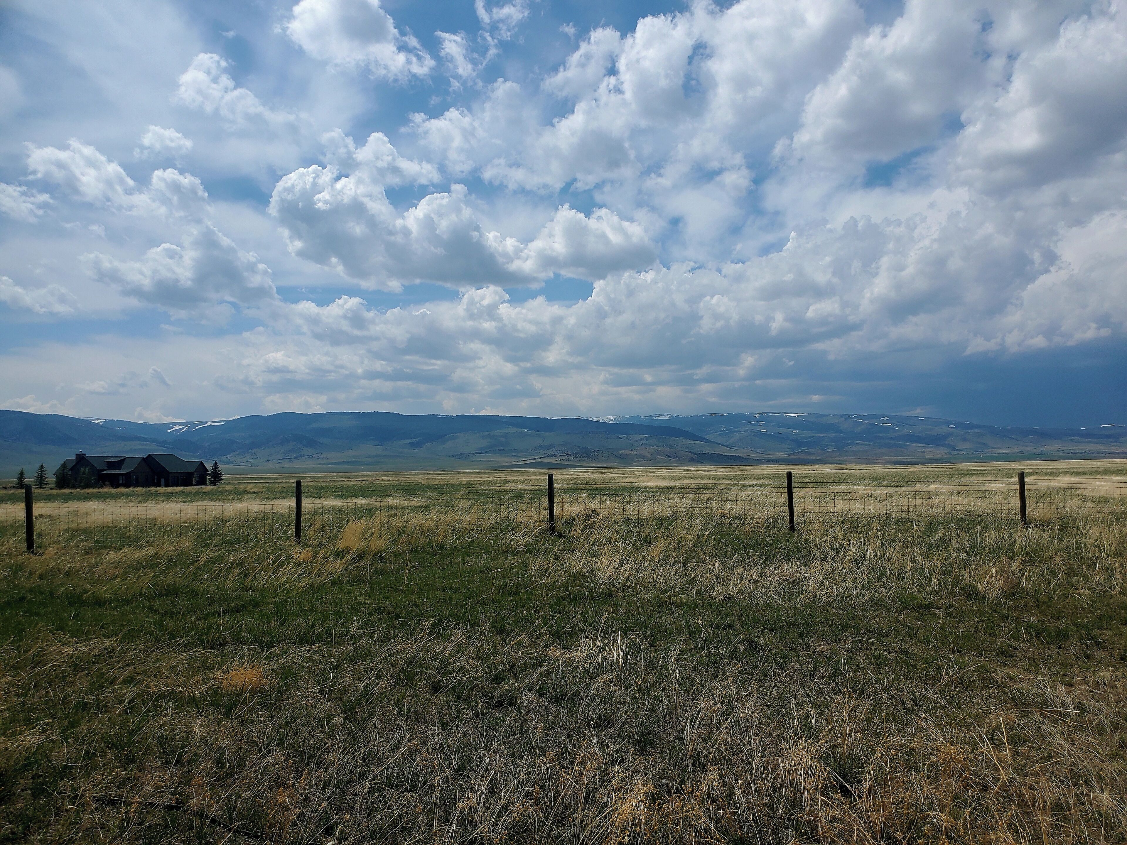 A rural landscape with a house, grassy field, and mountains in the background.