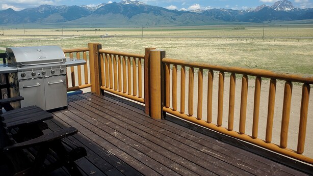 A deck with a grill and a table, overlooking a grassy field and mountains. - Dream Drift Motel (Cameron)