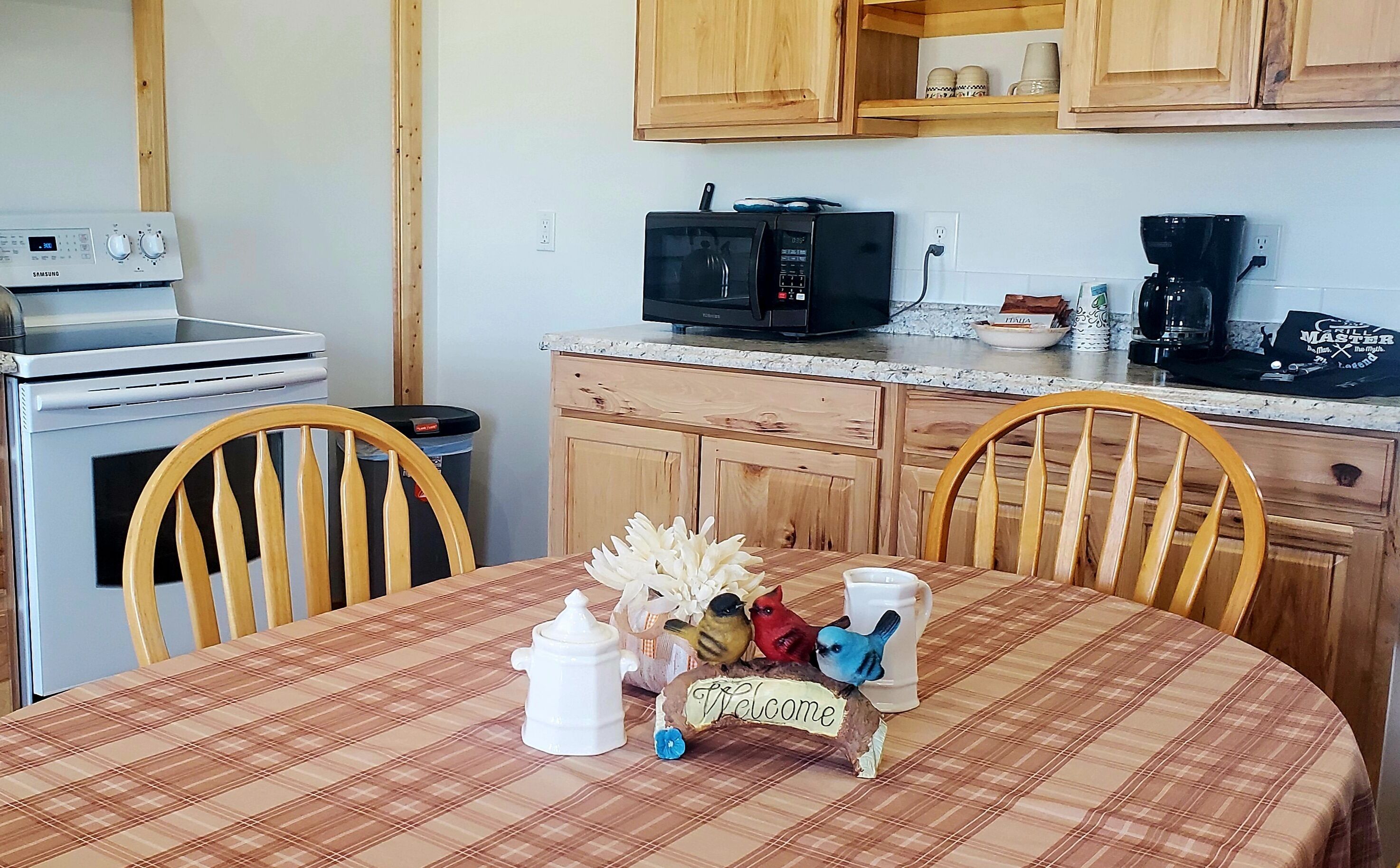 A kitchen with wooden cabinets, a microwave, a coffee maker, and a table with a plaid tablecloth.