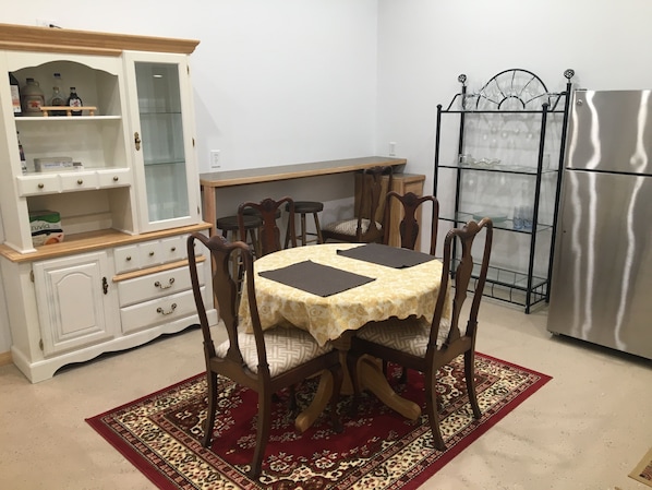 A dining area with a wooden table, chairs, a red patterned rug, a white cabinet with glass doors, and a stainless steel refrigerator. - Dream Drift Motel (Cameron)