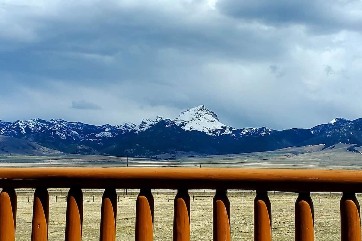 A mountain range with snow-capped peaks under a cloudy sky, viewed from a balcony with a railing.