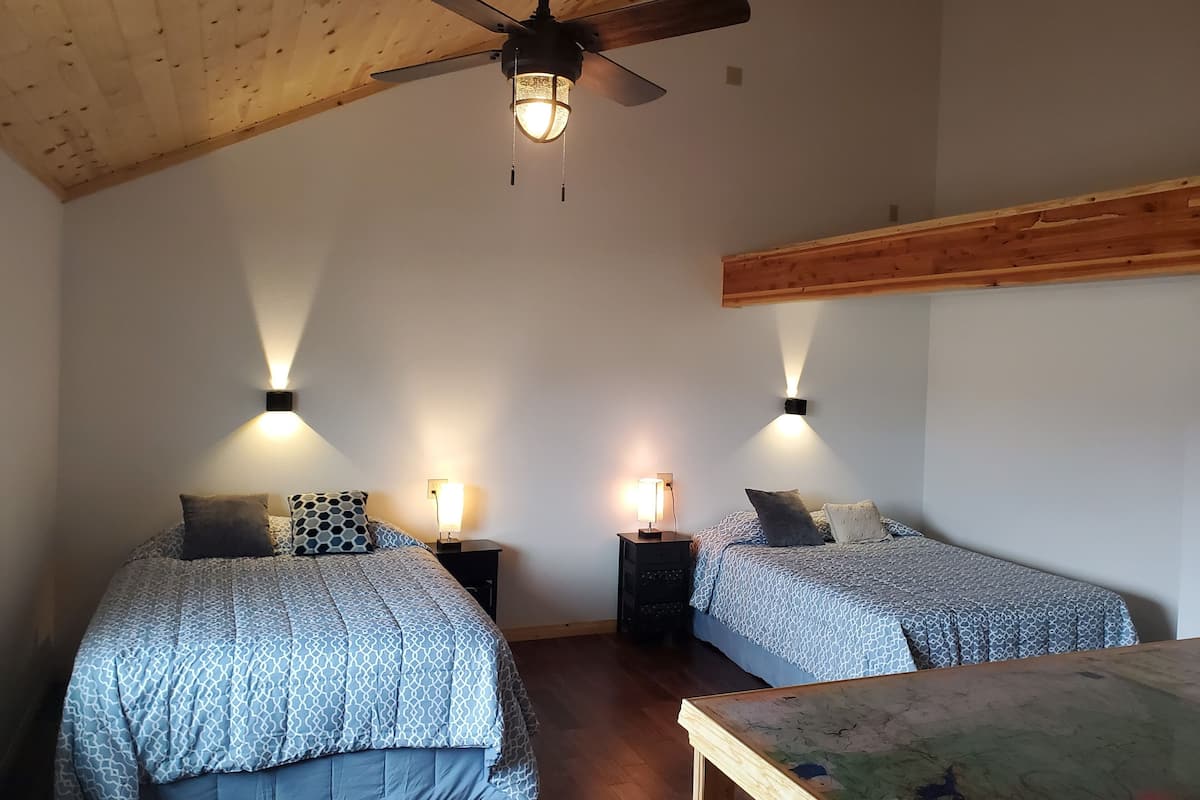 A bedroom with two beds, wooden ceiling beams, and wall-mounted lights.