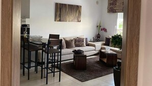 Una sala de estar moderna con comedor, que incluye un sofá, una mesa de centro y un cuadro en la pared.