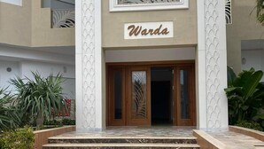 Entrada de un edificio con un letrero que dice "Warda" sobre una escalinata de mármol que lleva a una puerta de madera.