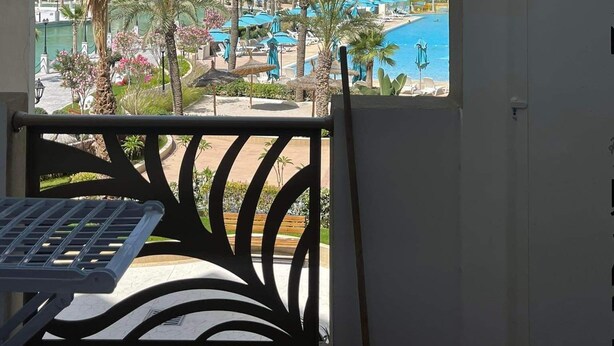 Un balcón con vista a un edificio de hotel, una piscina y palmeras.