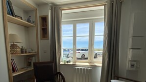 A living room with a view of parked cars, a bookshelf, a brown leather chair, a dark blue sofa, and a coffee table with a remote control.