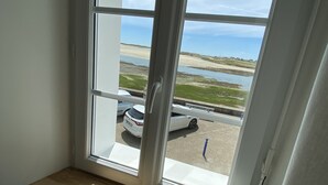 A room with a window overlooking a beach and parked cars.