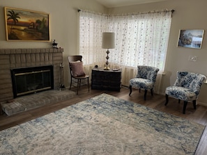 A living room with a fireplace, two patterned armchairs, a rug, and a painting on the wall.