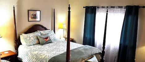 Una cama con dosel con colcha acolchada, dos almohadas, una mesita de noche con lámpara y un banco al pie de la cama.