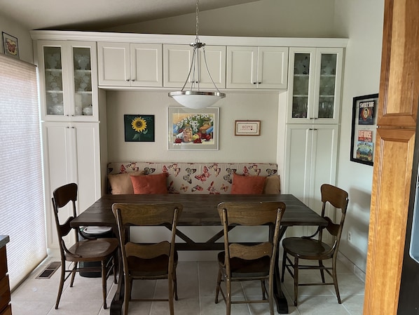 A dining area with a wooden table, chairs, a floral-patterned bench, and white cabinets with glass doors.