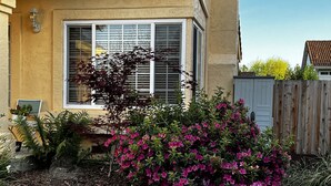 Una casa con un ventanal grande, una valla de madera y un jardín con flores rosadas.