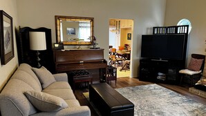 Una sala de estar con sofá, mesa de centro, televisor, piano y un comedor al fondo.