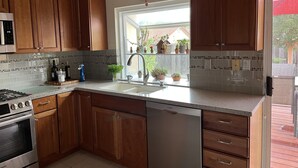 Una cocina con armarios de madera, lavavajillas Bosch, estufa de acero inoxidable y ventana con plantas en macetas.