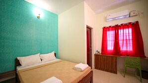 A neatly made bed with white linens, a wooden headboard, and a teal accent wall. - VR Inn (Puducherry)