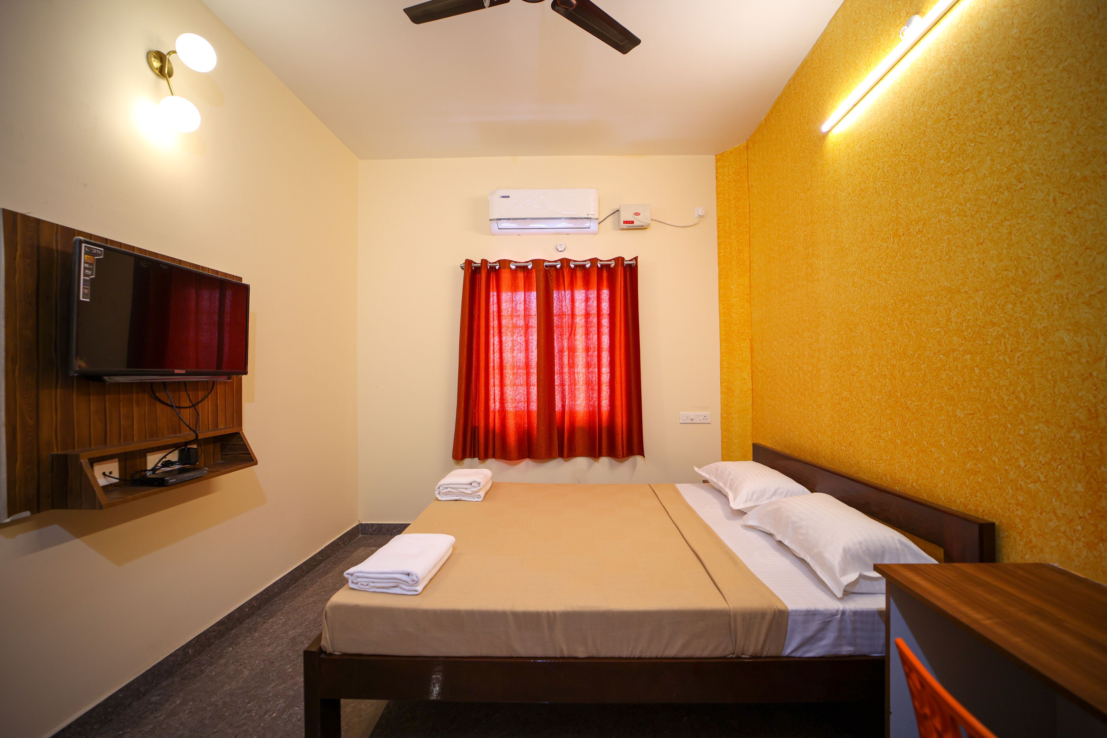 Una habitación de hotel con cama, televisor montado en la pared y equipo de aire acondicionado sobre la ventana.