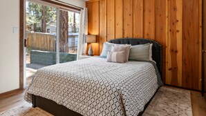 A bedroom with a large bed, wooden panel walls, a sliding glass door to a patio, and a nightstand with a lamp.