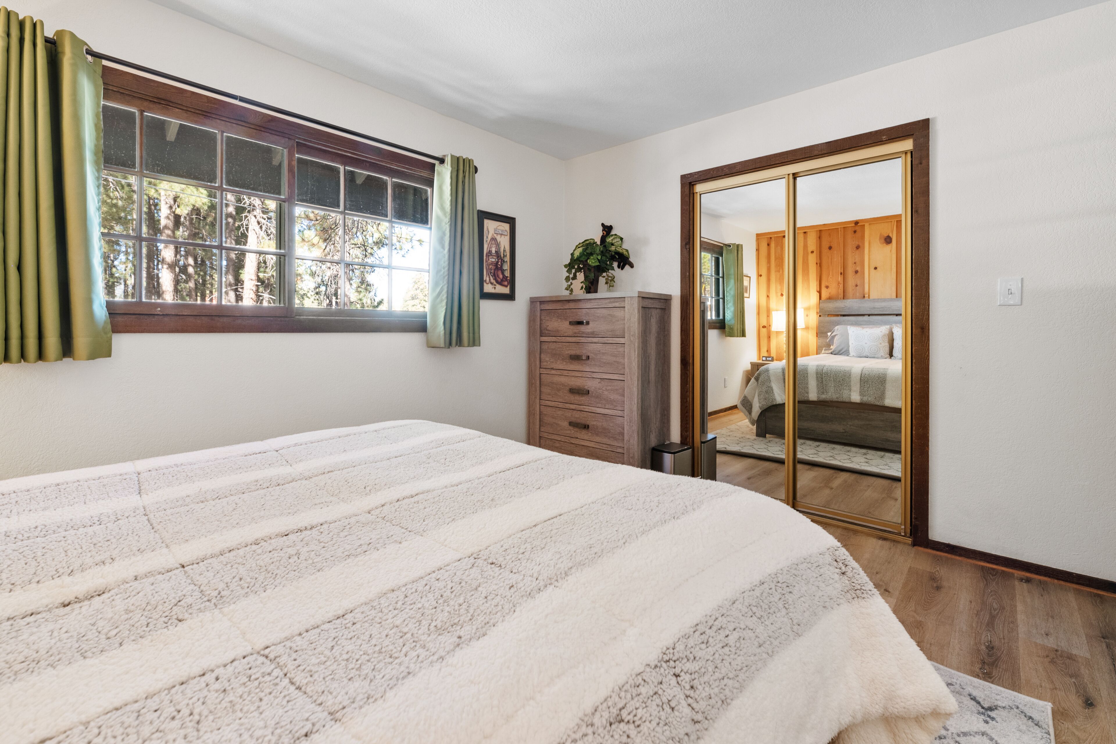 Une chambre à coucher avec un lit, une commode, un miroir et une fenêtre avec des rideaux.