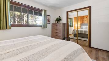 Une chambre à coucher avec un lit, une commode, un miroir et une fenêtre avec des rideaux.