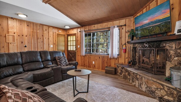 A cozy living room with a leather sectional sofa, a stone fireplace, and a large window with curtains.