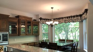 A kitchen with granite countertops, wooden cabinets, a dining table with chairs, a chandelier, and large windows with a view of trees. - Lake Fork house with private boat ramp, dock, fishing light, kayak, 8 acres land (Alba)