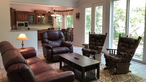 A spacious living room with leather sofas, a coffee table, and a dining area with chairs. A kitchen with wooden cabinets and a chandelier is visible in the background. - Lake Fork house with private boat ramp, dock, fishing light, kayak, 8 acres land (Alba)