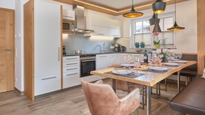 A modern kitchen with white cabinets, a built-in oven, and a dining area with a wooden table set for six. - Luxury chalet with sauna and garden (Piesendorf)