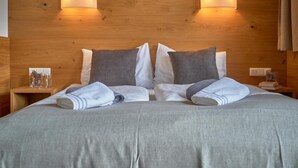 A neatly made bed with a grey bedspread and two pillows, wooden headboard with wall-mounted lights, and a small bedside table with a glass and a book. - Luxury chalet with sauna and garden (Piesendorf)