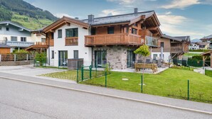 A modern two-story house with a stone facade, wooden balconies, and a well-maintained lawn. - Luxury chalet with sauna and garden (Piesendorf)