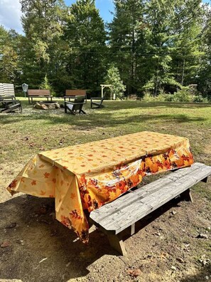 Une table de pique-nique recouverte d’une nappe à motifs floraux, entourée de bancs et d’arbres, dans un cadre de parc.