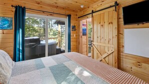 A wooden cabin room with a bed, a TV, and a sliding glass door leading to an outdoor deck. - Hemlocks Over Muir-WiFi, Firepit, Hot Tub, located in Muir Valley (Rogers)