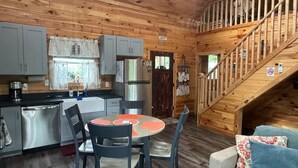 A cozy cabin interior with a wooden interior, a dining area with a round table and chairs, a kitchen with modern appliances, and a staircase leading to an upper level. - Hemlocks Over Muir-WiFi, Firepit, Hot Tub, located in Muir Valley (Rogers)