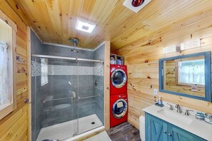 Une petite salle de bain dotée d’une douche à parois de verre, d’un lave-linge rouge et d’un lavabo avec un miroir.