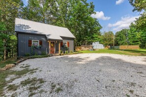 Une cabane rustique avec une allée en gravier et une clôture en bois en arrière-plan.