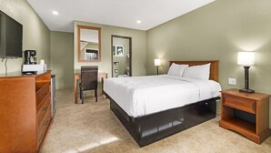 A hotel room with a bed, a desk, a chair, a dresser, a mirror, and a nightstand with a lamp. - Safari Inn - Chico (Chico)