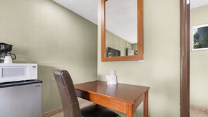 A kitchenette with a microwave, a coffee maker, and a refrigerator. There is a wooden table with a chair and a tissue box. A mirror hangs on the wall. - Safari Inn - Chico (Chico)