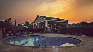 A swimming pool with a covered pavilion, a fenced area, and a sunset in the background. - Safari Inn - Chico (Chico)