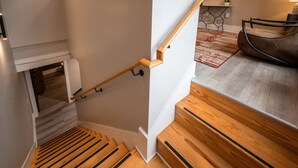 Una escalera de madera con barandilla, un rellano pequeño y vista a una sala de estar con sofá y alfombra.
