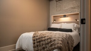 Un dormitorio con cama, cabecera, estante en la pared y una puerta.