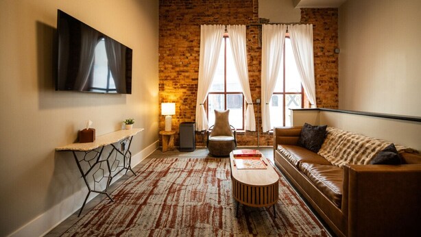 Un salón con pared de ladrillo, televisor de pantalla plana, sofá, mesa de centro y lámpara.
