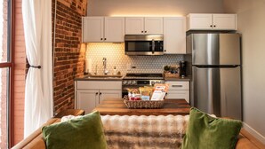 A kitchen with white cabinets, a stainless steel refrigerator, and a microwave. There is a basket on the counter with snacks. - 1 Bedroom Suite Downtown Elkin Yadkin Valley (Elkin)