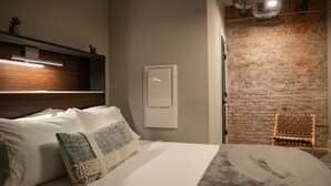 A bed with white linens and a patterned throw, a wooden headboard, a wall-mounted light, a framed picture, and a brick wall. - 2 Bedroom Townhouse Downtown Elkin Yadkin Valley (Elkin)