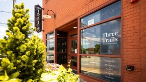 Un immeuble portant une enseigne indiquant « Three Trails Boutique Loft Suites » et affichant une liste de commodités, notamment des cuisines entièrement équipées, un système d’enregistrement autonome, une connexion Wi-Fi rapide, l’acceptation des animaux de compagnie et la possibilité de séjours flexibles.