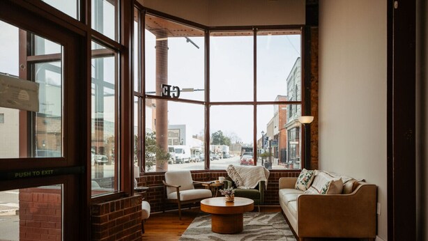 A cozy room with a brick wall, a large window, a sofa, a chair, and a coffee table. - Studio Suite Yadkin Valley Downtown Elkin (Elkin)