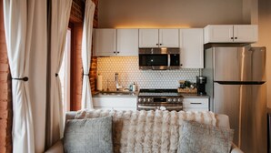 A modern kitchen with white cabinets, a stainless steel refrigerator, a microwave, and a gas stove. - Studio Suite Yadkin Valley Downtown Elkin (Elkin)