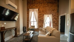 Een woonkamer met een bakstenen muur, een flatscreen televisie, een bank, een salontafel en een open haard.