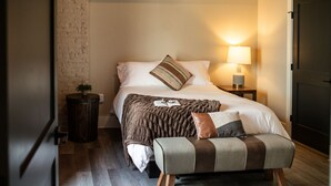 Een slaapkamer met een bed, nachtkastje, lamp en een deur.