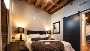 Un dormitorio con cama, lámparas de noche, una puerta y una pared de ladrillo.