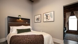 Une chambre à coucher comprenant un lit, une tête de lit, une table de chevet, une lampe fixée au mur et deux œuvres d’art encadrées.